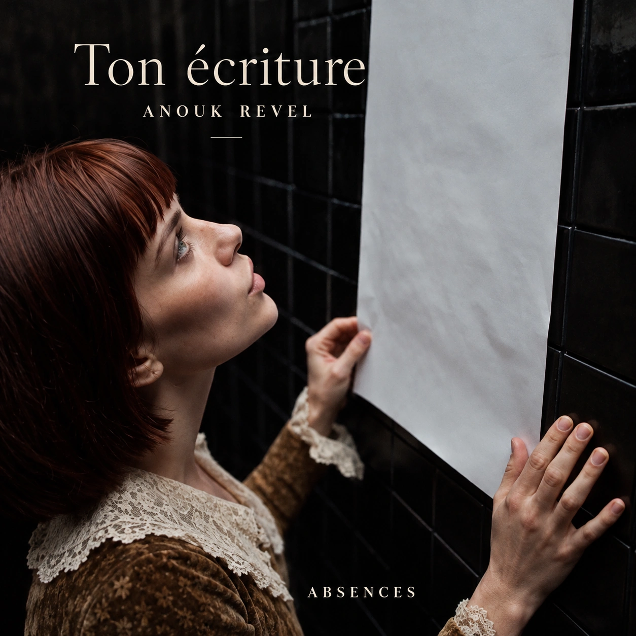 Anouk touche une feuille blanche sur un mur carrelé sombre.